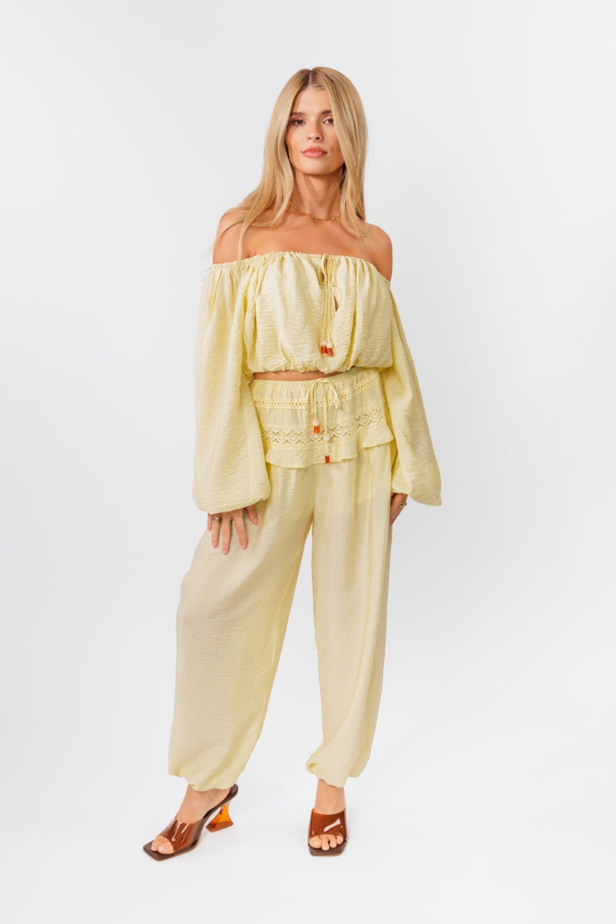 Woman wearing a yellow off-shoulder top and yellow balloon pants on a white background