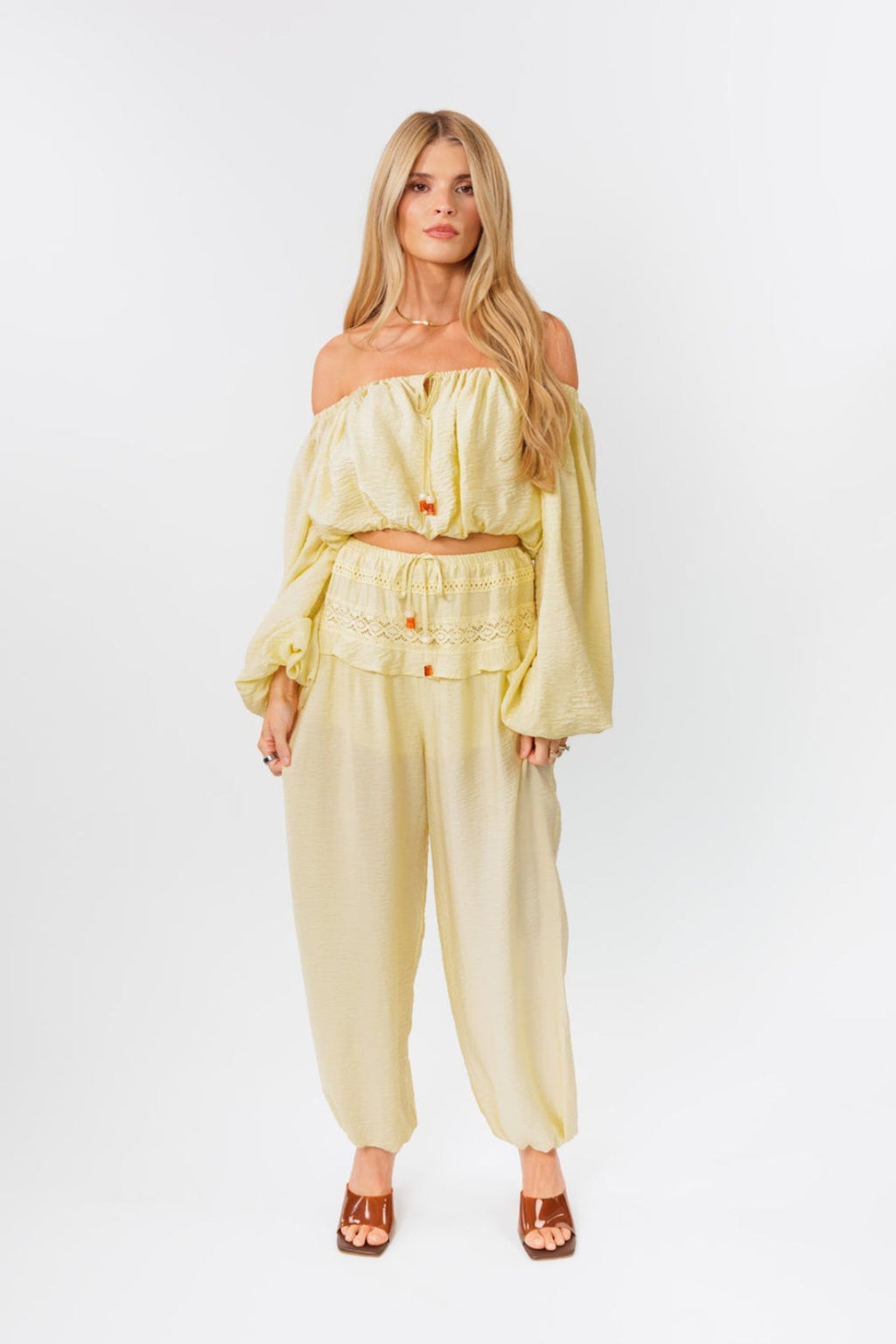 Woman wearing a yellow off-shoulder top and yellow balloon pants on a white background