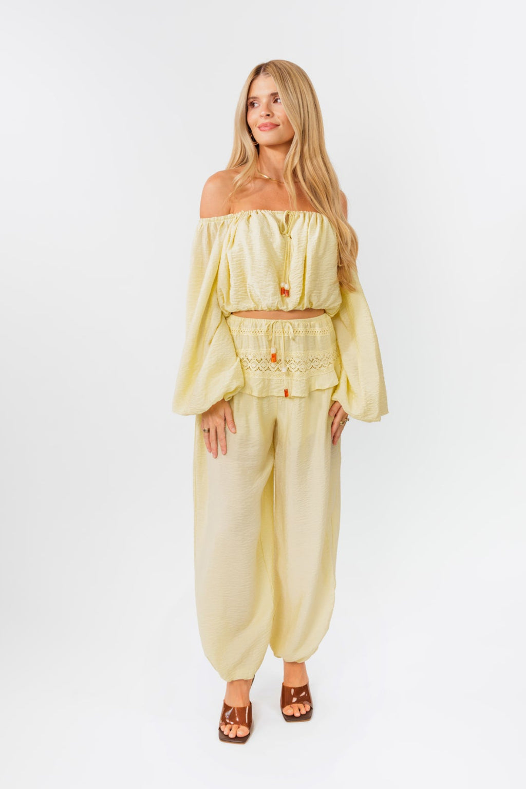 Woman wearing a yellow off-shoulder top and yellow balloon pants on a white background