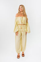 Woman wearing a yellow off-shoulder top and yellow balloon pants on a white background