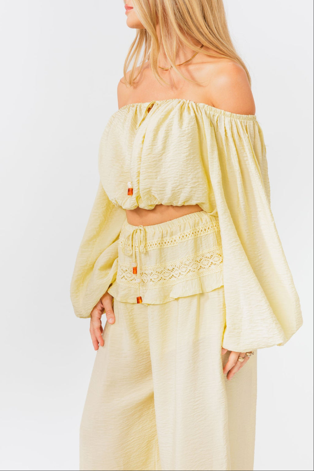 Woman wearing a yellow off-shoulder top and yellow balloon pants on a white background