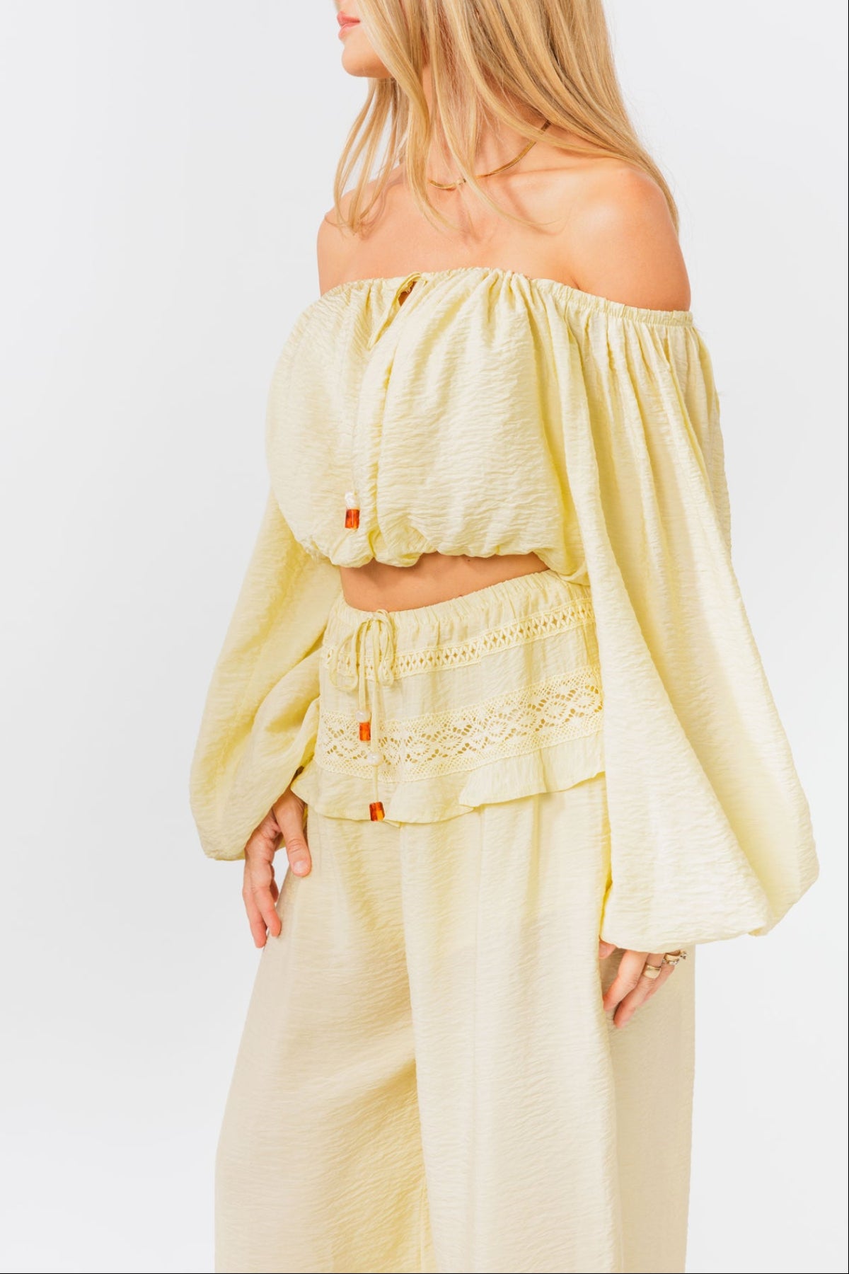 Woman wearing a yellow off-shoulder top and yellow balloon pants on a white background