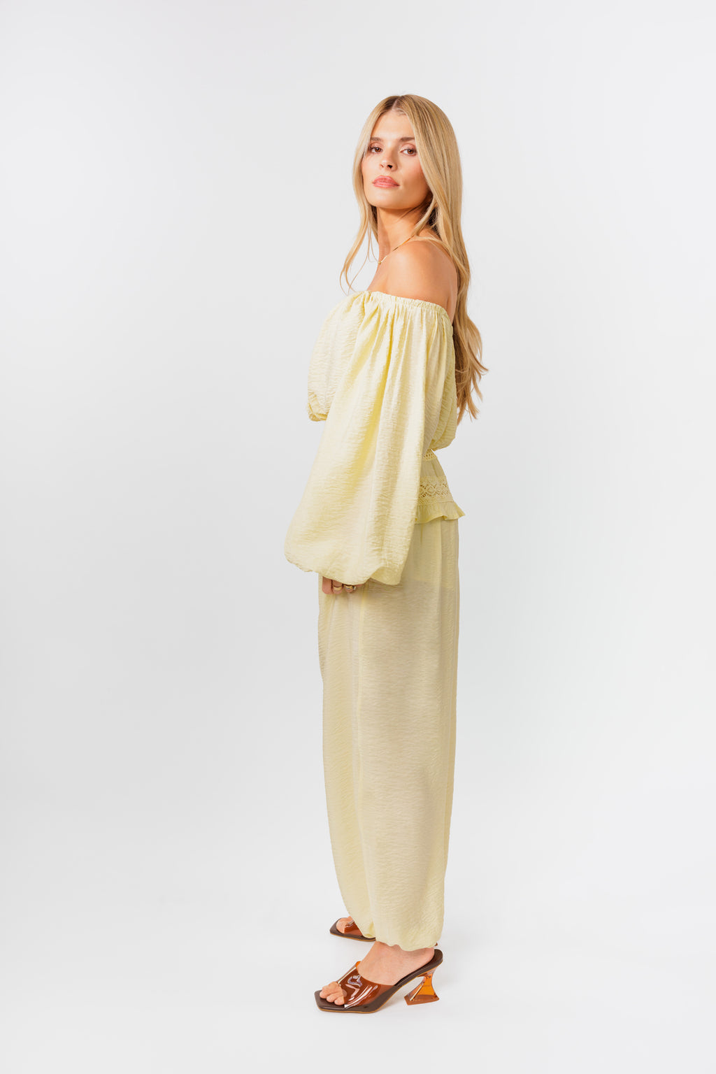 Woman wearing a yellow off-shoulder top and yellow balloon pants on a white background