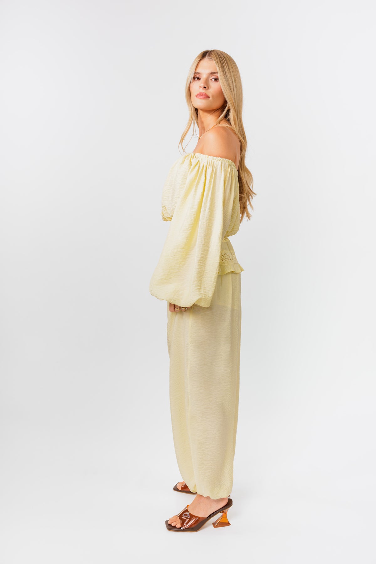 Woman wearing a yellow off-shoulder top and yellow balloon pants on a white background