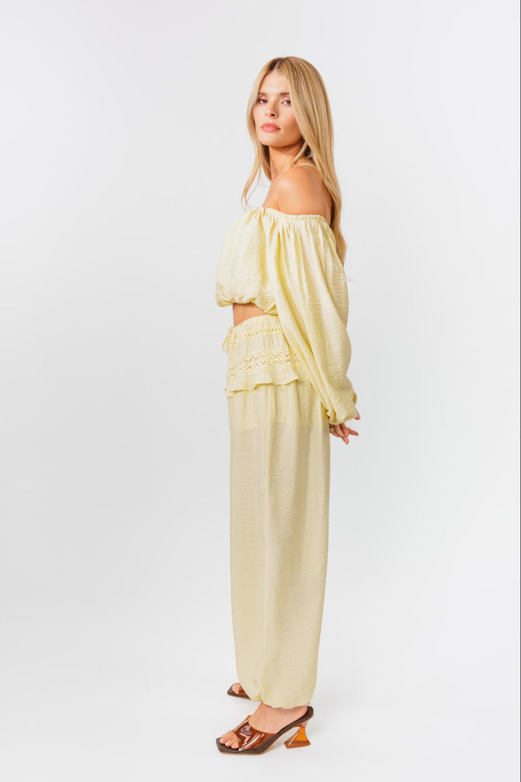 Woman wearing a yellow off-shoulder top and yellow balloon pants on a white background