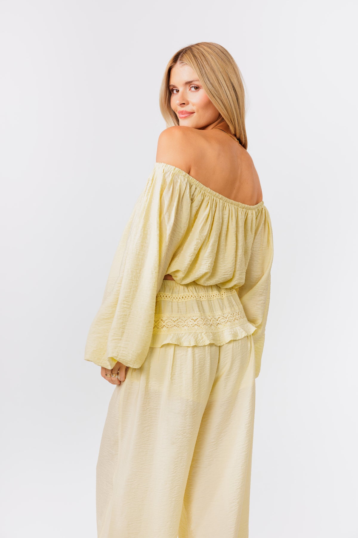 Woman wearing a yellow off-shoulder top and yellow balloon pants on a white background