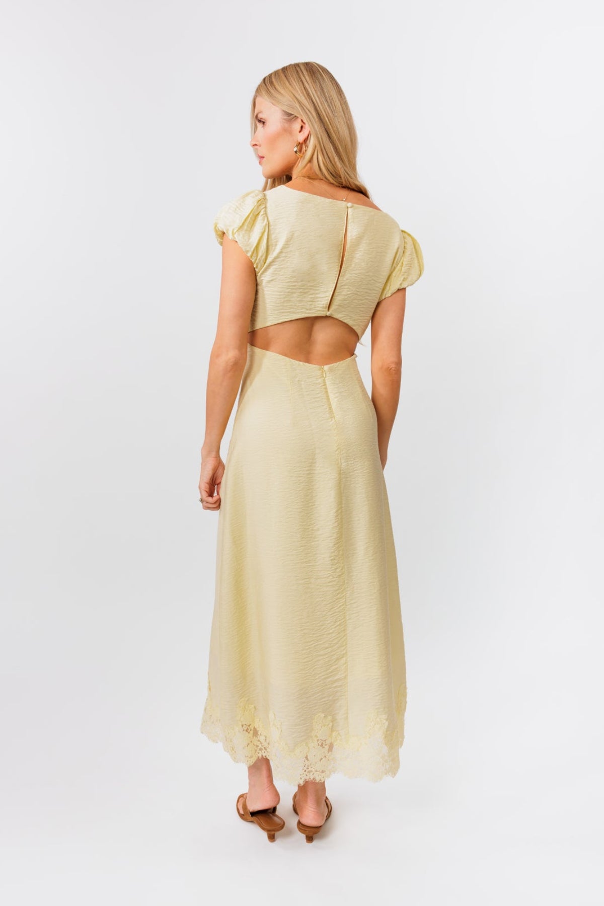 Woman wearing a light yellow dress with a cutout back on a white background
