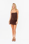Woman wearing a brown mini skort and lace tank with studded details on a white background