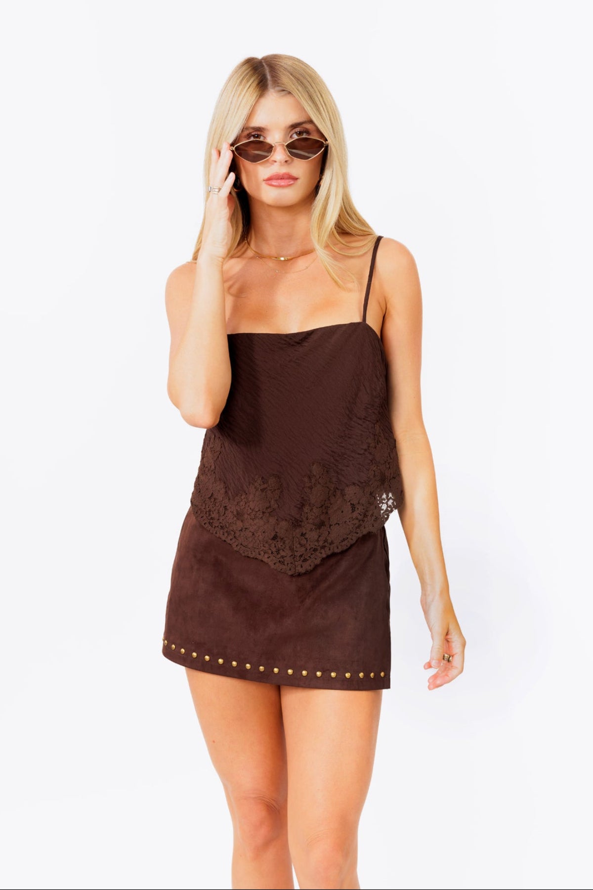 Woman wearing a brown mini skort and lace tank with studded details on a white background