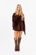 Woman wearing a brown fringe dress and cowboy boots on a white background