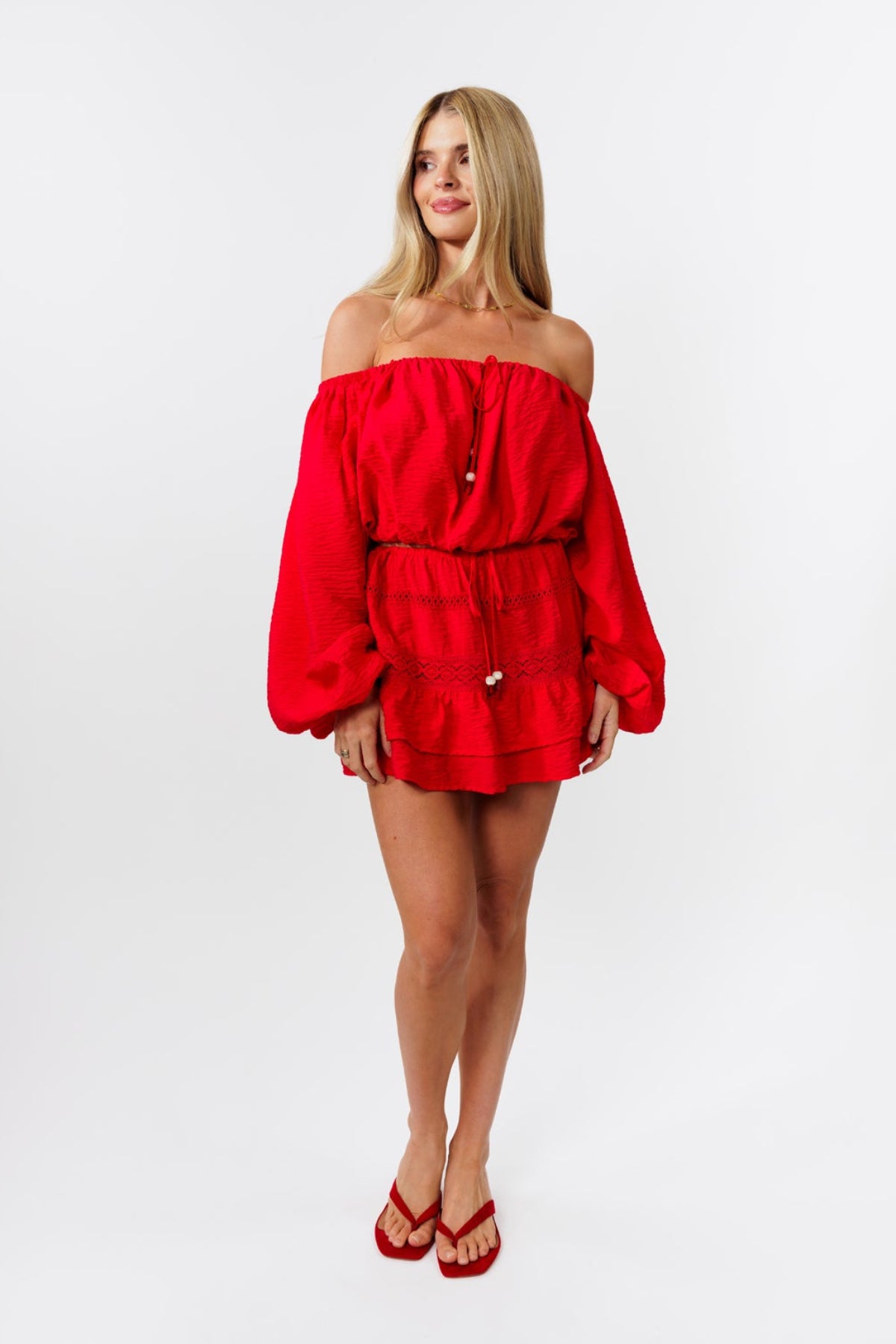 Woman wearing a red off-shoulder top and red skirt on a white background