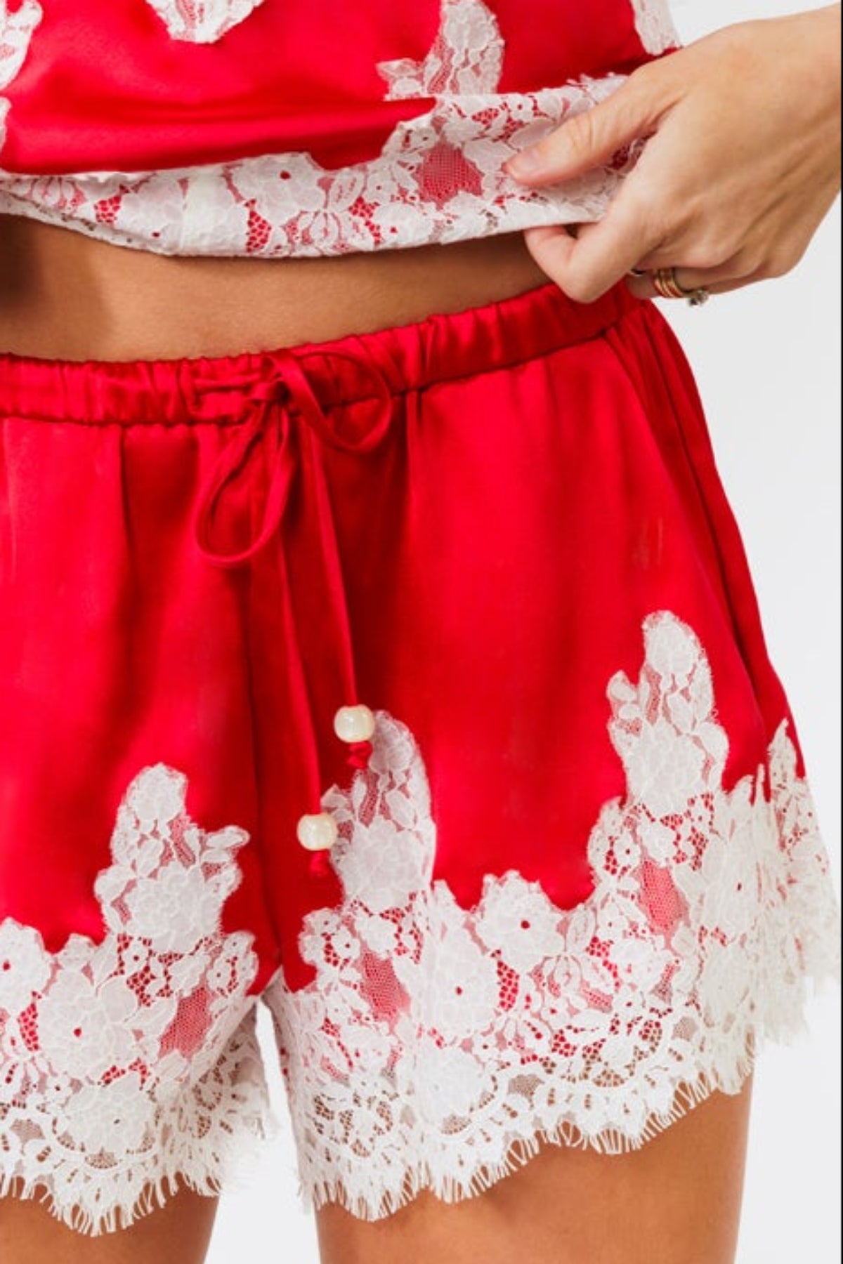 Woman wearing a red satin tank and short with white lace trim on a white background