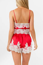 Woman wearing a red satin tank and short with white lace trim on a white background