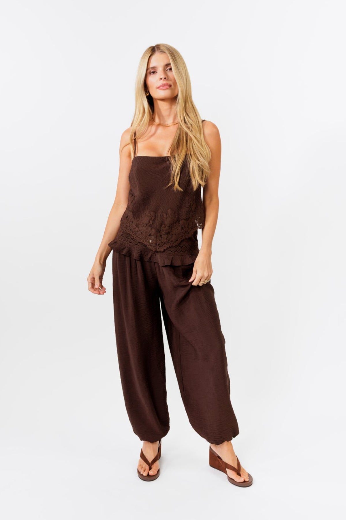 Woman wearing a brown tank with lace details and a brown suede skort on a white background