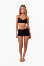 A model wearing black ribbed boyshorts and a matching bralette against a plain white background.