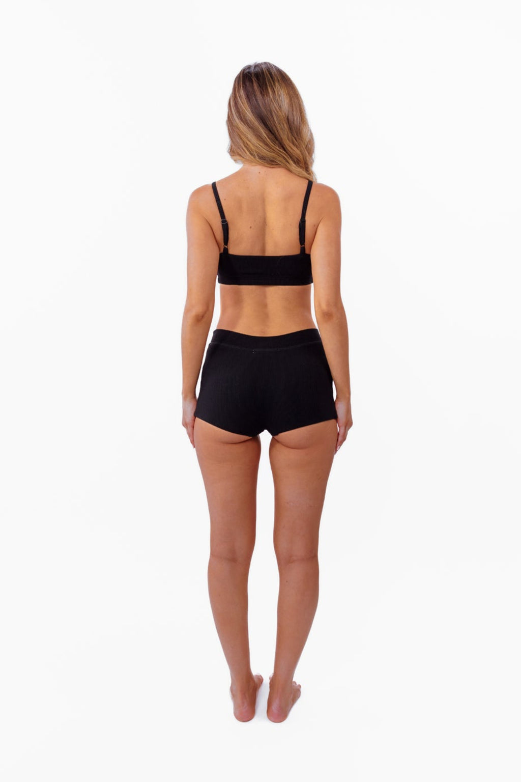 model wearing black ribbed bralette with matching thong standing in front of a white backdrop
