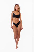A model wearing a black ribbed thong and matching bralette against a plain white background.