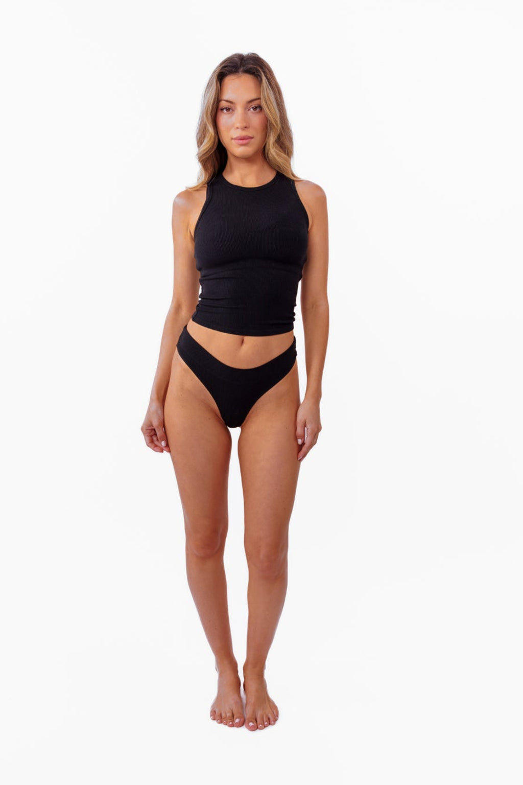 model wearing black ribbed tank with matching thong standing in front of a white backdrop