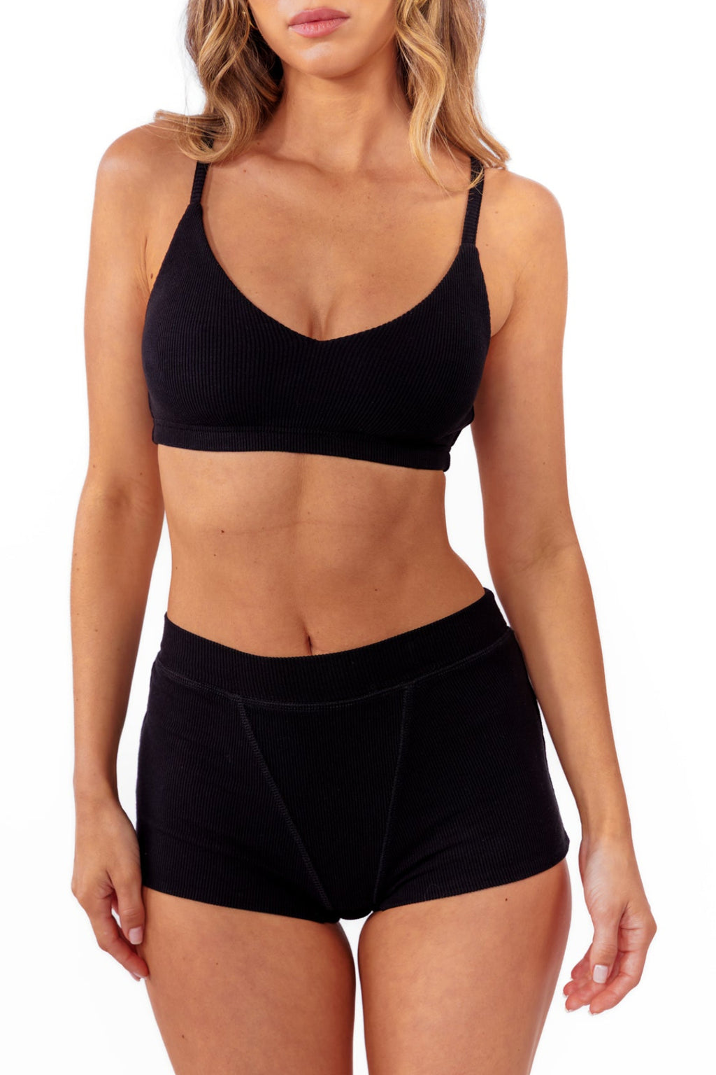 A model wearing black ribbed boyshorts and a matching bralette against a plain white background.