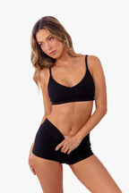 model wearing black ribbed bralette with matching thong standing in front of a white backdrop