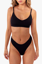 model wearing black ribbed bralette with matching thong standing in front of a white backdrop