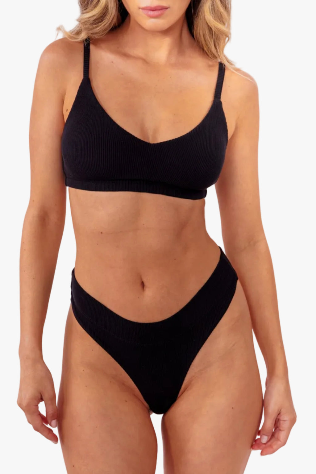A model wearing a black ribbed thong and matching bralette against a plain white background.