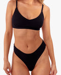 A model wearing a black ribbed thong and matching bralette against a plain white background.