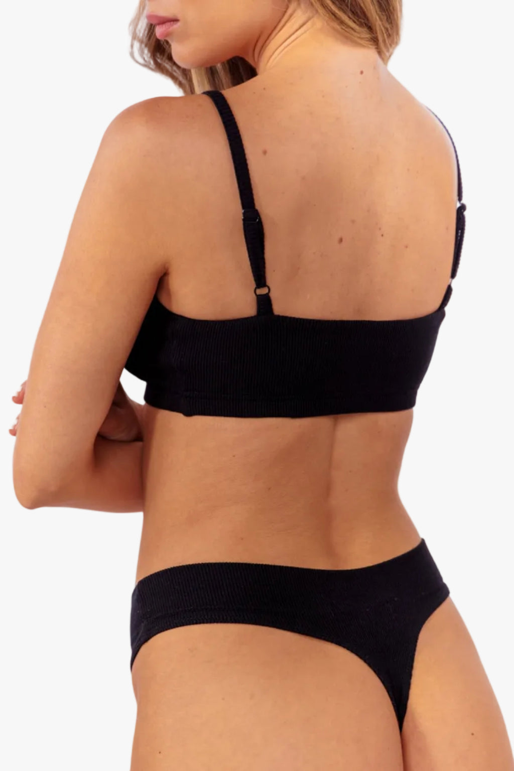 model wearing black ribbed bralette with matching thong standing in front of a white backdrop