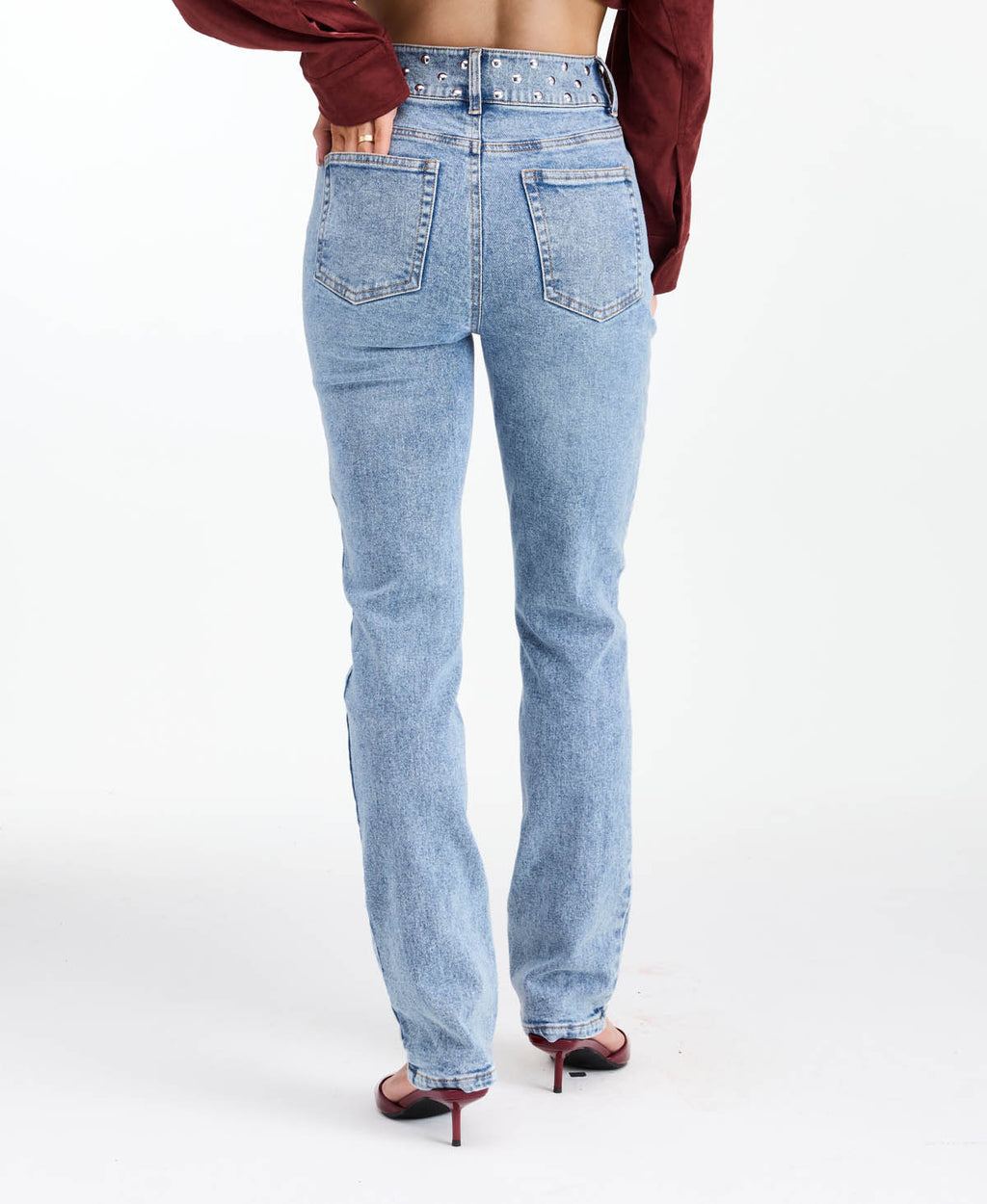 Model wearing high waisted skinny straight leg jeans with a studded waistband paired with kitten heels.