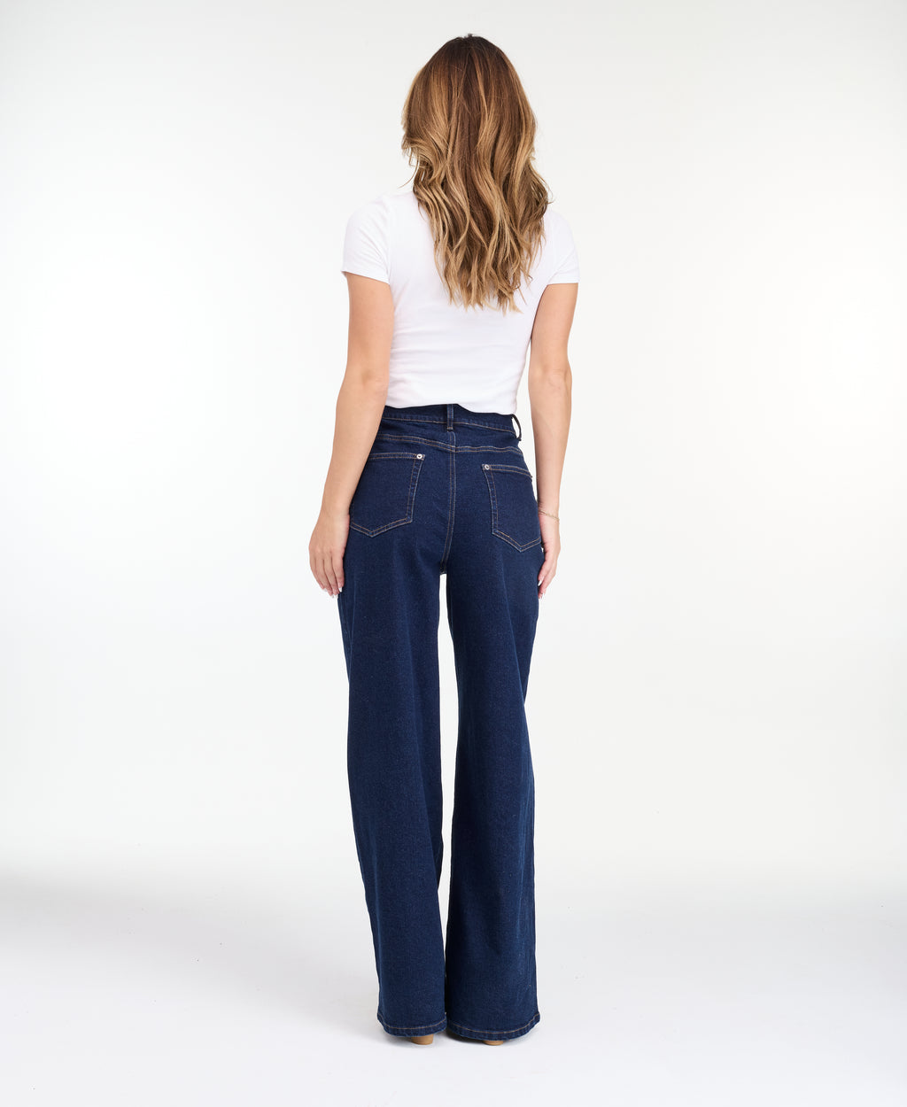A model wearing dark blue wide-leg denim jeans with a high waist and front pleats, shown from the waist down on a white studio background.