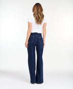 A model wearing dark blue wide-leg denim jeans with a high waist and front pleats, shown from the waist down on a white studio background.