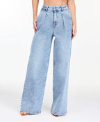 A woman modeling a light-wash blue denim outfit consisting of wide-leg jeans, a white ribbed top, and an open light blue denim jacket, photographed against a seamless white studio background.