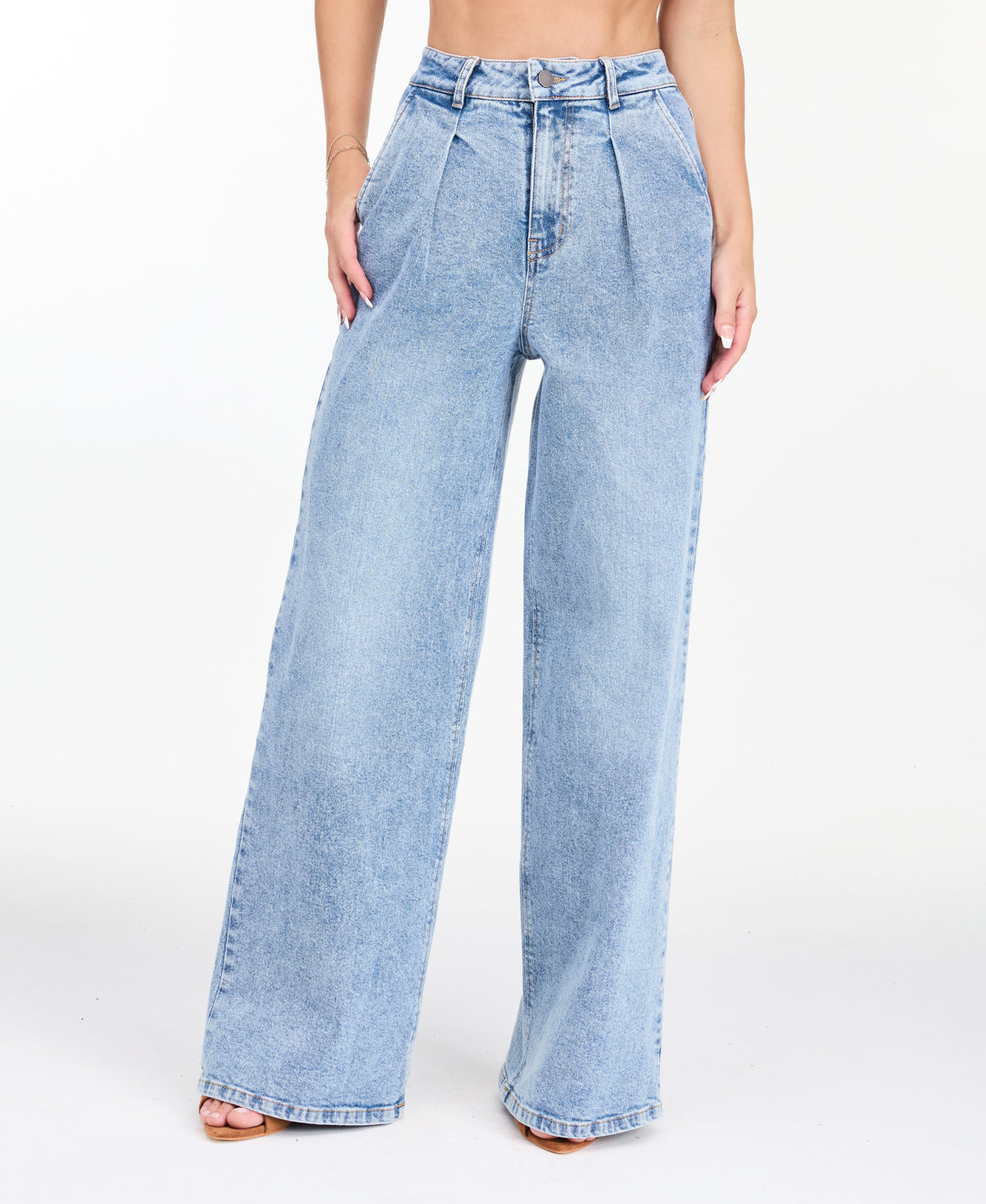 A woman modeling a light-wash blue denim outfit consisting of wide-leg jeans, a white ribbed top, and an open light blue denim jacket, photographed against a seamless white studio background.