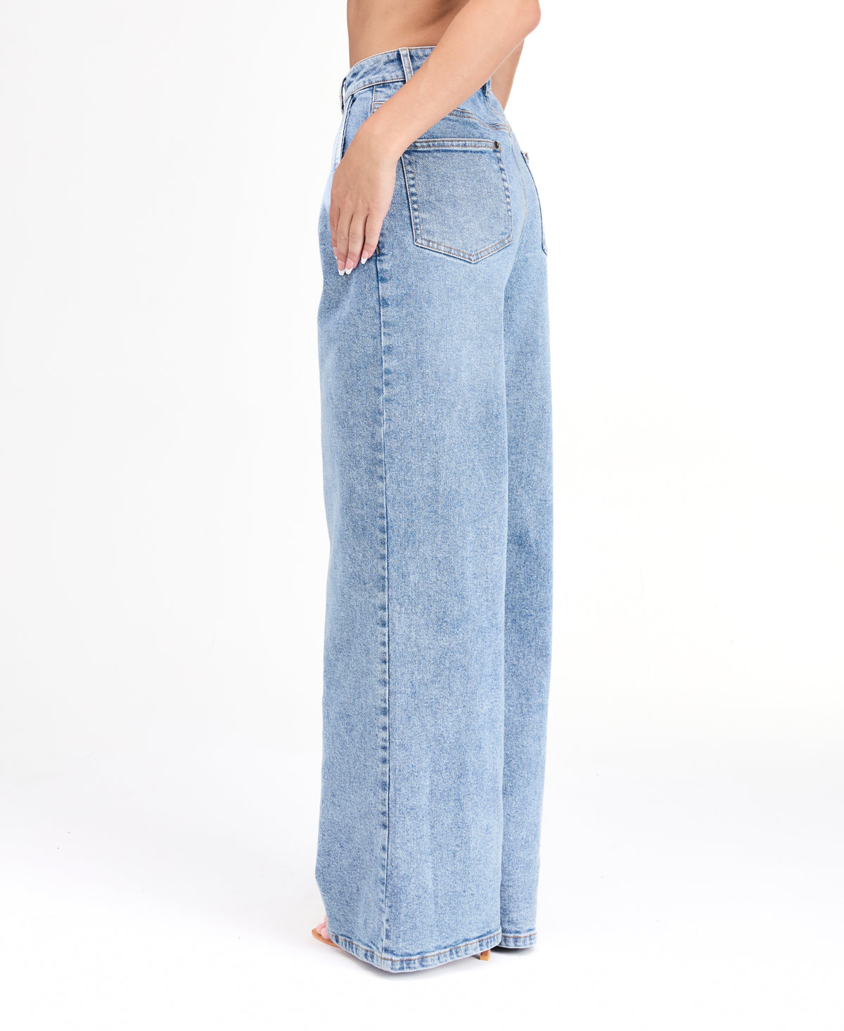 A woman modeling a light-wash blue denim outfit consisting of wide-leg jeans, a white ribbed top, and an open light blue denim jacket, photographed against a seamless white studio background.