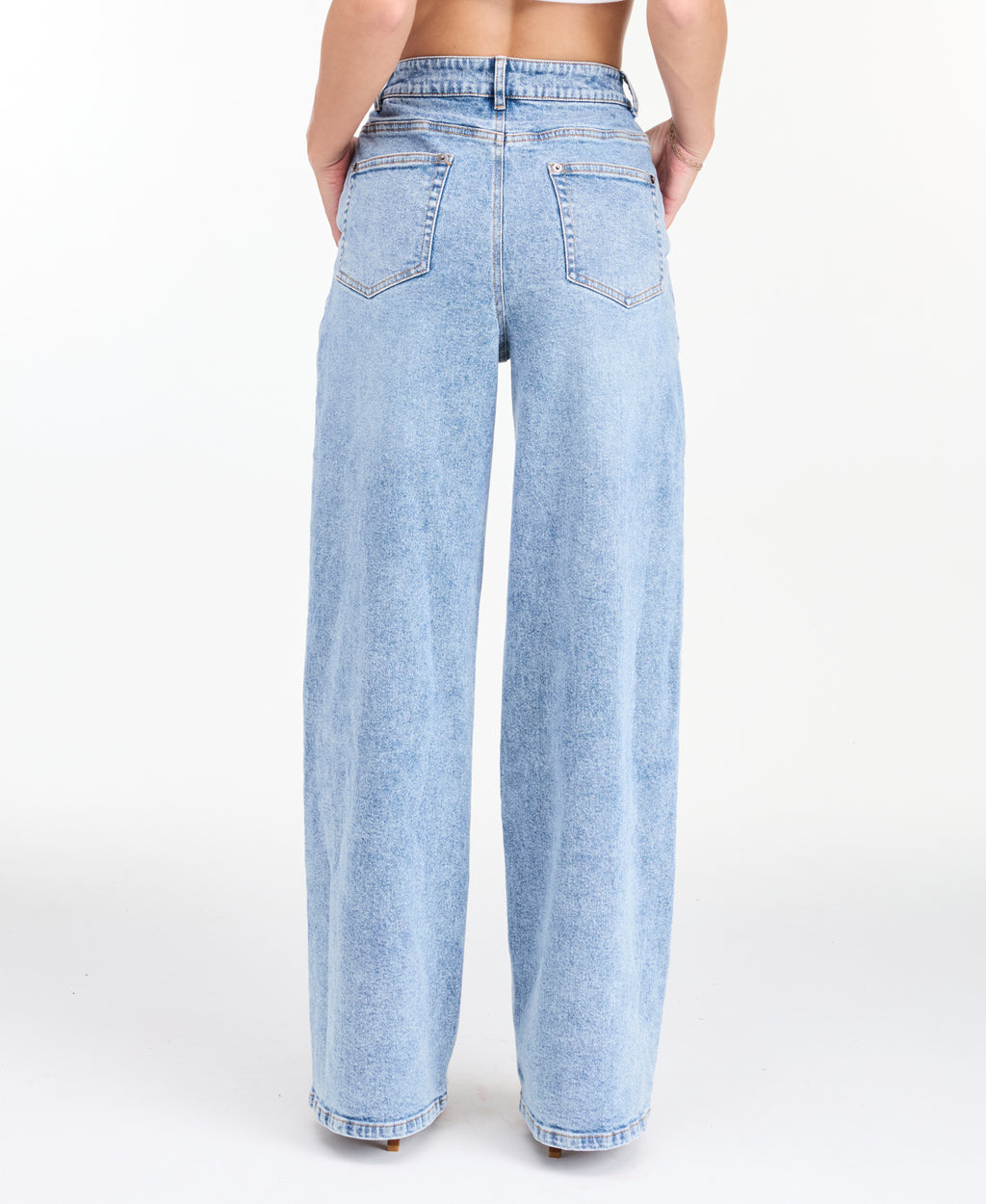 A woman modeling a light-wash blue denim outfit consisting of wide-leg jeans, a white ribbed top, and an open light blue denim jacket, photographed against a seamless white studio background.
