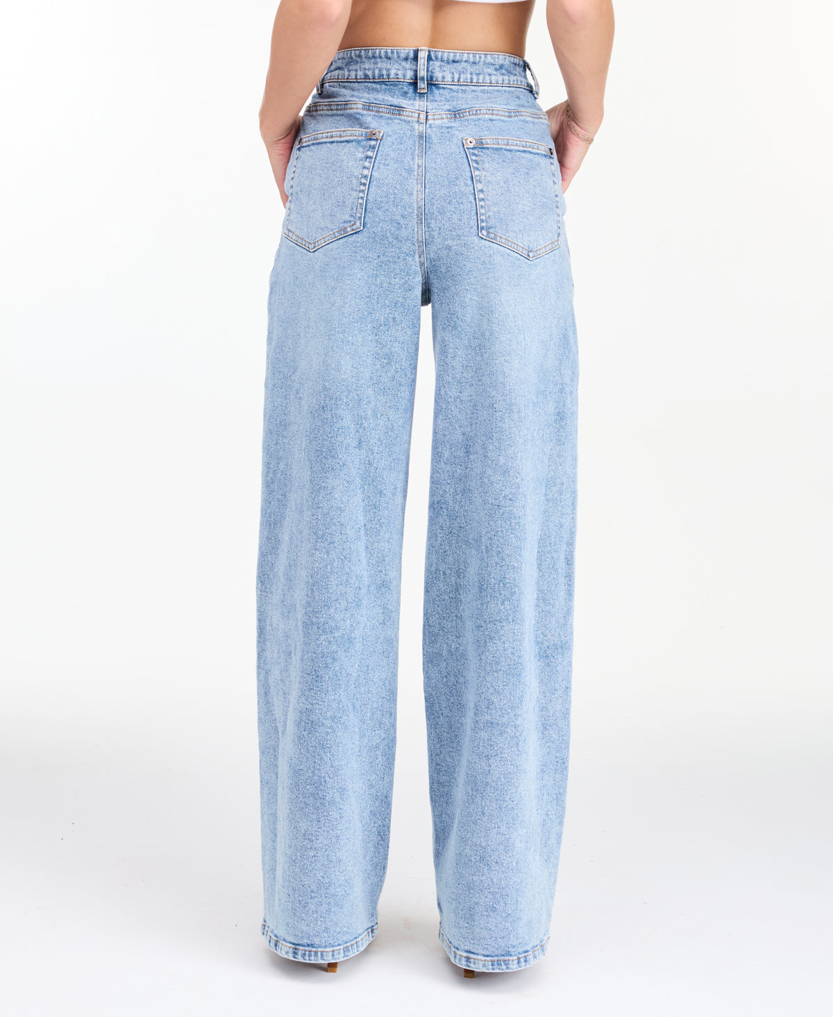 A woman modeling a light-wash blue denim outfit consisting of wide-leg jeans, a white ribbed top, and an open light blue denim jacket, photographed against a seamless white studio background.