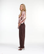Model wearing a pink snake print top with brown suede pants and brown kitten heels standing against a white back drop