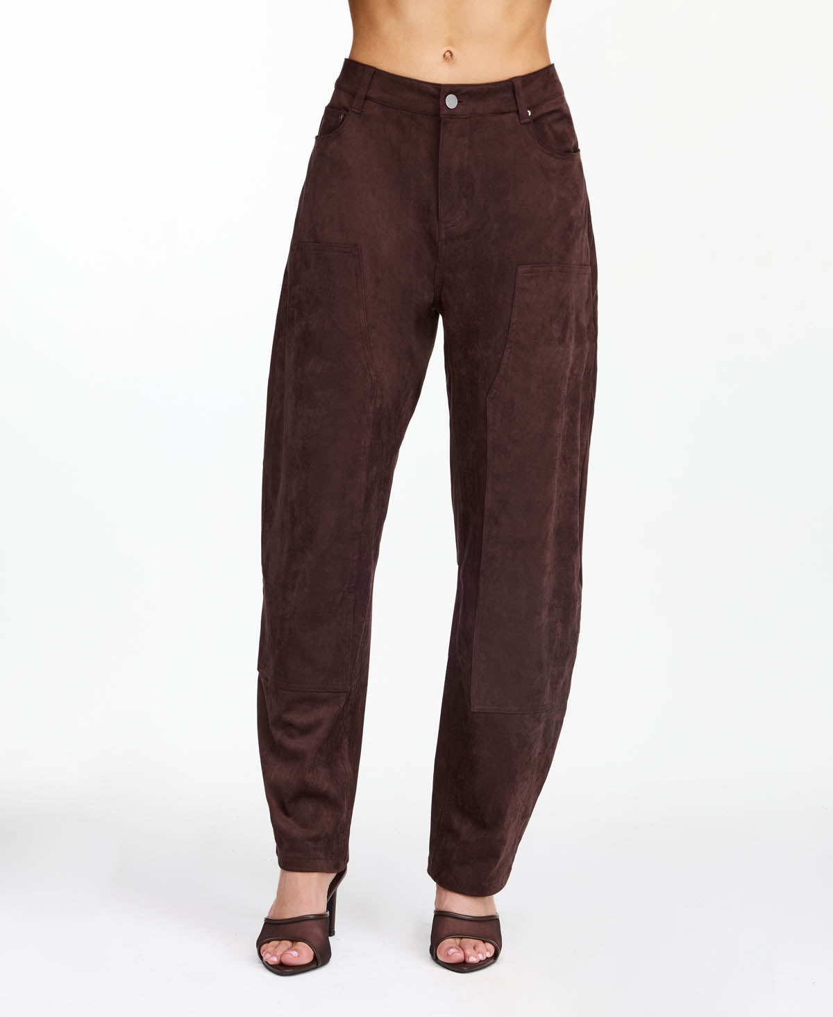 Model wearing brown faux suede barrel pants with brown kitten heels and a snake print top standing in front of a white back drop
