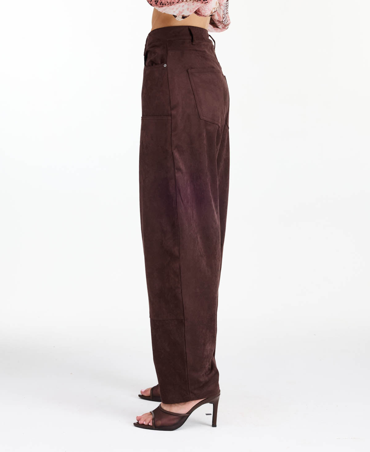 Model wearing brown faux suede barrel pants with brown kitten heels and a snake print top standing in front of a white back drop