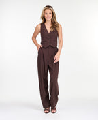 A model is shown from the waist down wearing high-waisted, wide-leg brown trousers with thin vertical pinstripes, paired with brown  heels against a plain white studio background.