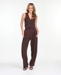 A model is shown from the waist down wearing high-waisted, wide-leg brown trousers with thin vertical pinstripes, paired with brown  heels against a plain white studio background.