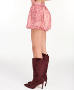 A model is shown from the waist down wearing a pink and red floral print bubble short paired with dark burgundy suede knee-high boots, against a plain white studio background.