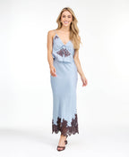 A woman modeling a light blue tank and midi skirt  with brown floral embroidery and appliqué on the bodice and hem, set against a plain white studio background.