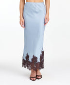 Model wearing a blue satin midi skirt with brown lace appliqué at the hem