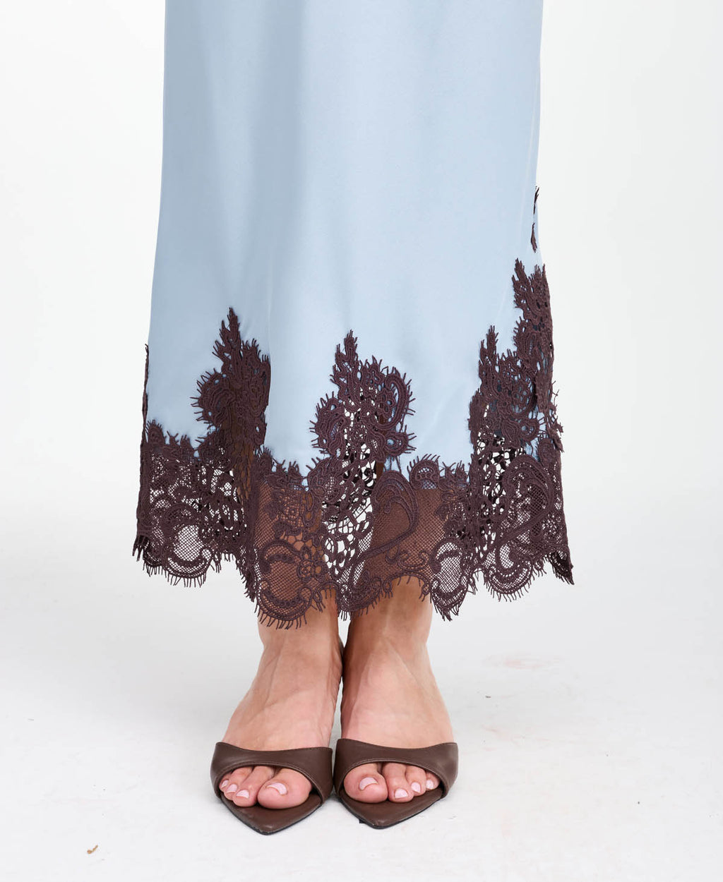 A woman modeling a light blue tank and midi skirt  with brown floral embroidery and appliqué on the bodice and hem, set against a plain white studio background.