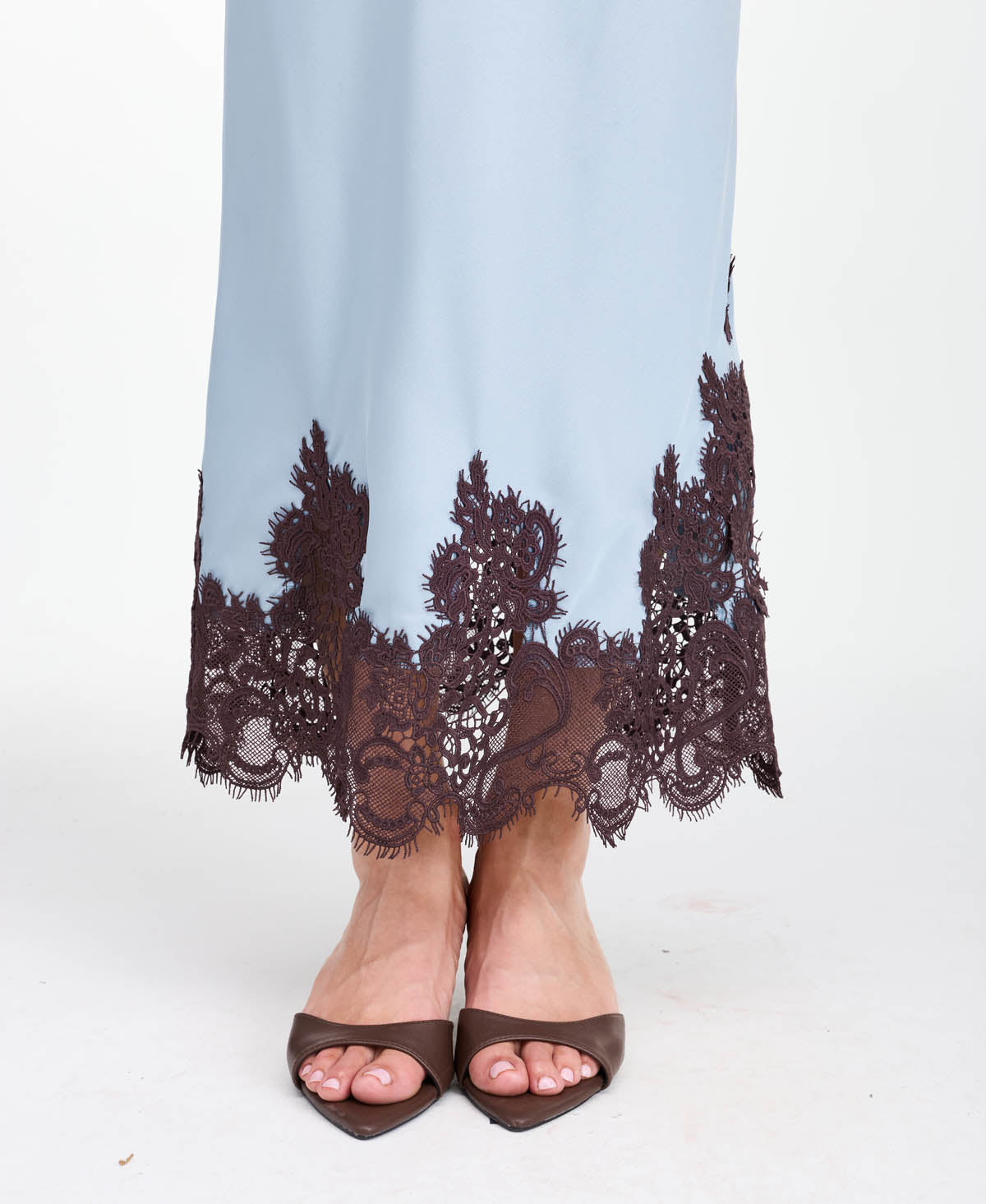 A woman modeling a light blue tank and midi skirt  with brown floral embroidery and appliqué on the bodice and hem, set against a plain white studio background.