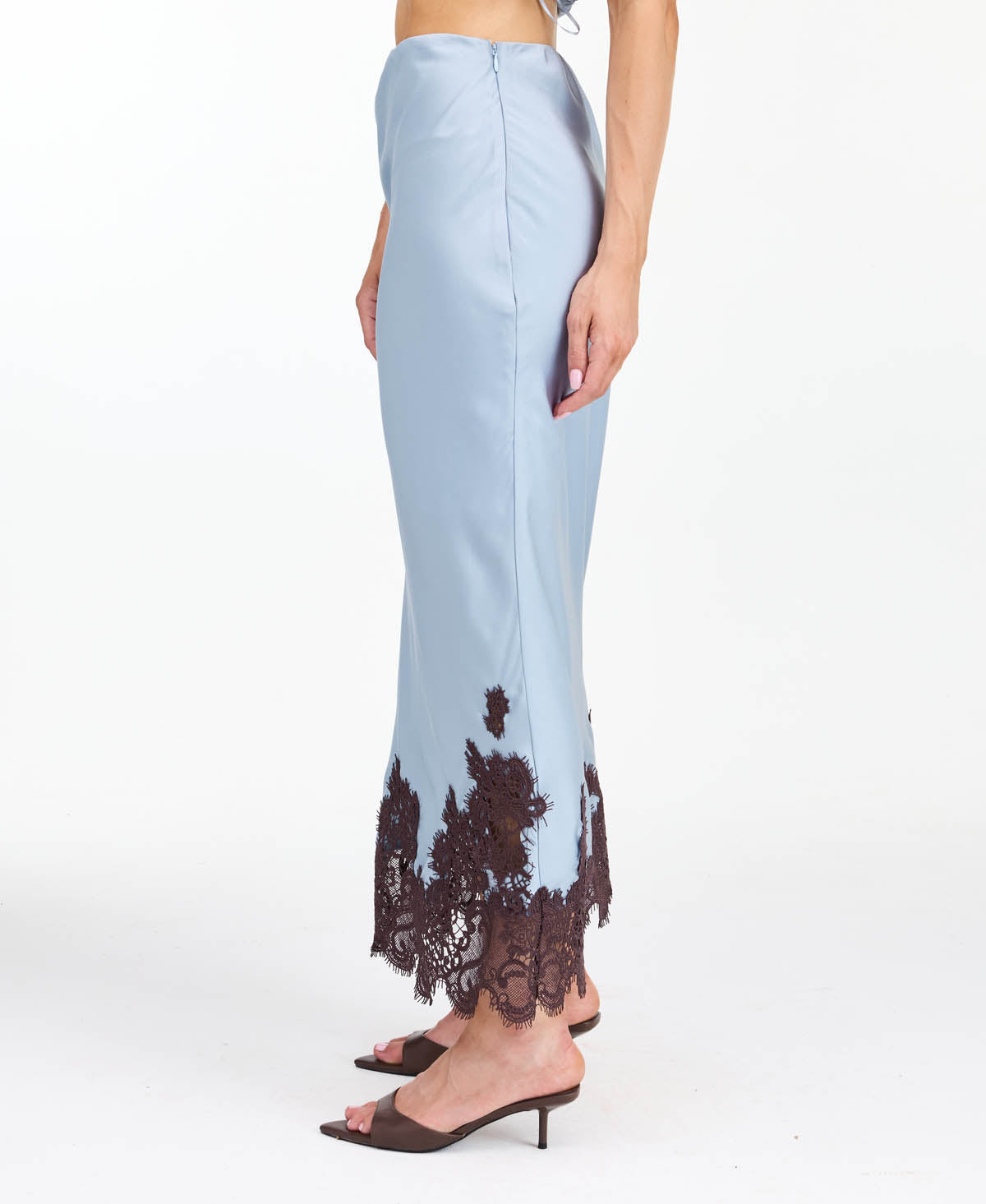 A woman modeling a light blue tank and midi skirt  with brown floral embroidery and appliqué on the bodice and hem, set against a plain white studio background.