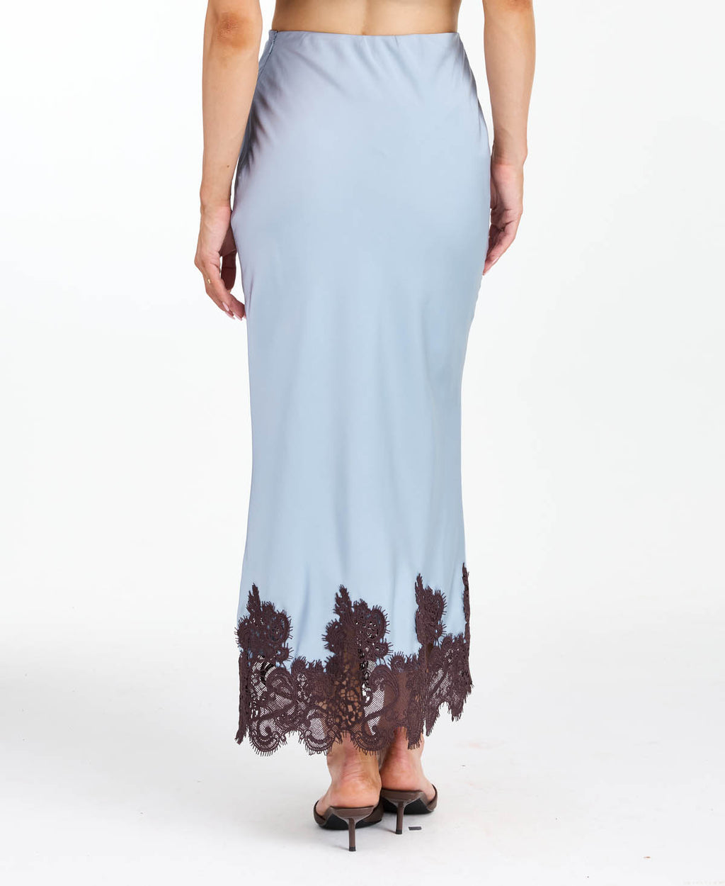 A woman modeling a light blue tank and midi skirt  with brown floral embroidery and appliqué on the bodice and hem, set against a plain white studio background.