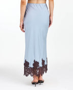A woman modeling a light blue tank and midi skirt  with brown floral embroidery and appliqué on the bodice and hem, set against a plain white studio background.