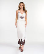 A woman modeling a white midi with dark brown lace detailing on the bodice of tank and hem, standing against a plain white studio background.